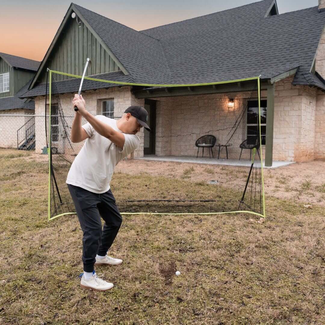 Person practicing golf swing with a 10' x 7' Premium Golf Practice Net in backyard setting.