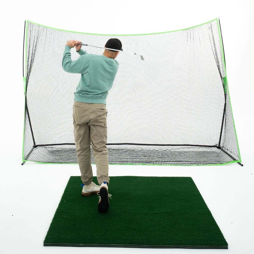 Golfer practicing with a 10' x 7' Premium Golf Practice Net indoors, hitting golf balls in training.
