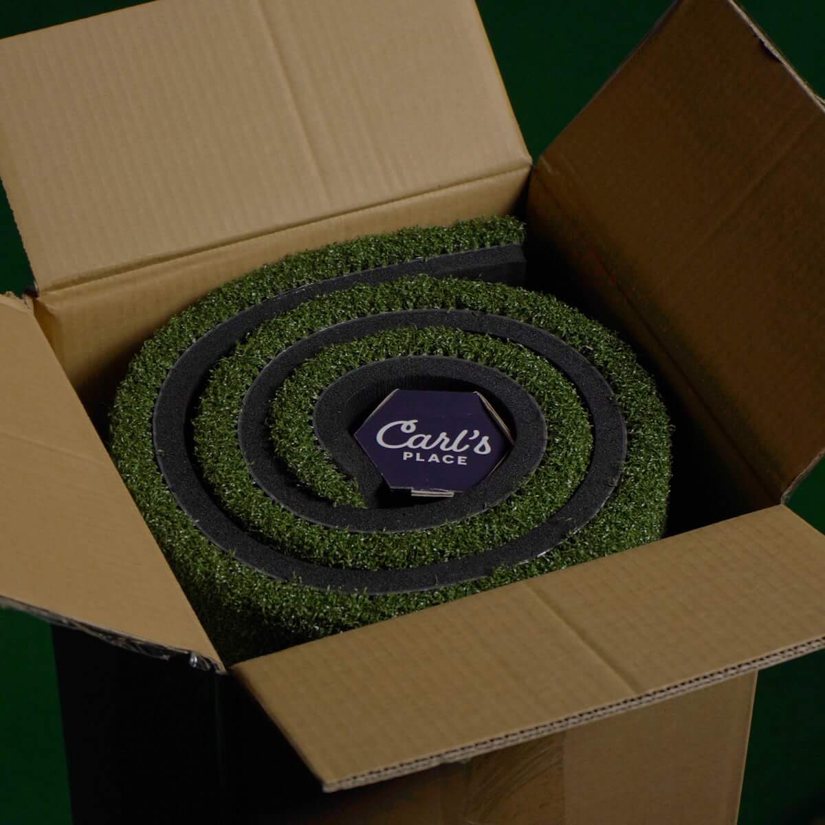 Carl's Place HotShot Golf Hitting Mat rolled up inside a cardboard box, showcasing premium practice surface for golf.