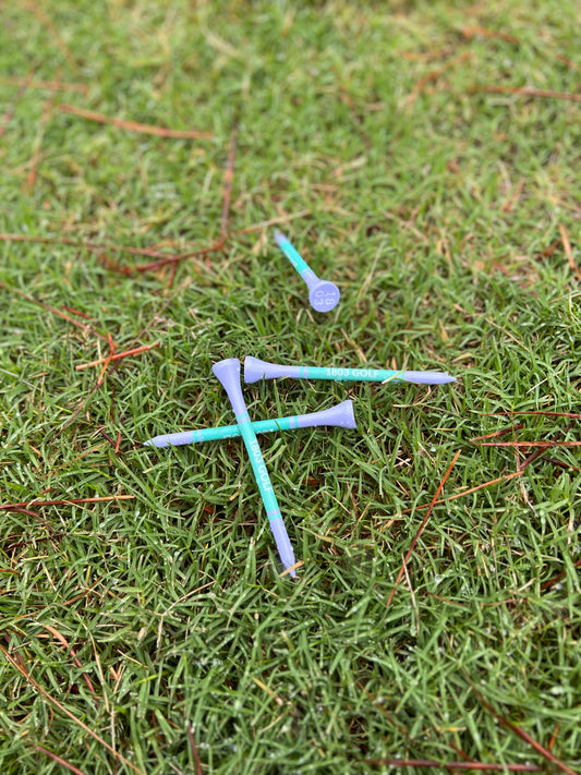 1803 Golf Royal Purple Tees in light purple and turquoise on grass, featuring '1803' in the tee caps.