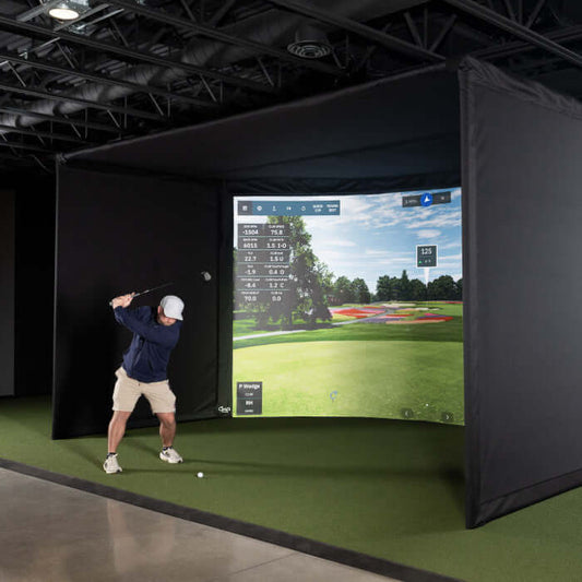 User hitting a golf ball in the Carl's Place Curved Golf Enclosure Kit with High-Contrast Gray Impact Screen.