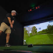 Golfer using a launch monitor in a golf simulator; Carl's Uneekor EYE XO2 Protective Case enhances experience.