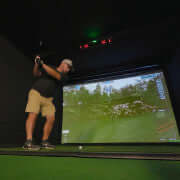 Golfer practicing swing indoors with a simulator displaying a golf course backdrop using Carl's Uneekor EYE XO2 Protective Case. 