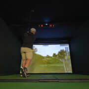 Golfer using a simulator with Carl’s Uneekor EYE XO2 Protective Case in a dark room with a screen.